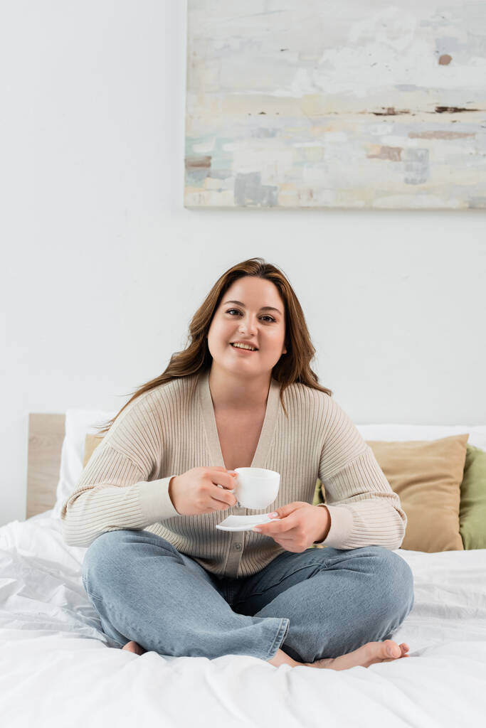 Feliz más tamaño mujer sosteniendo taza de café en la cama  - Foto, Imagen