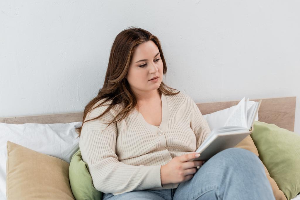 Young body positive woman reading book on bed at home  - Photo, Image