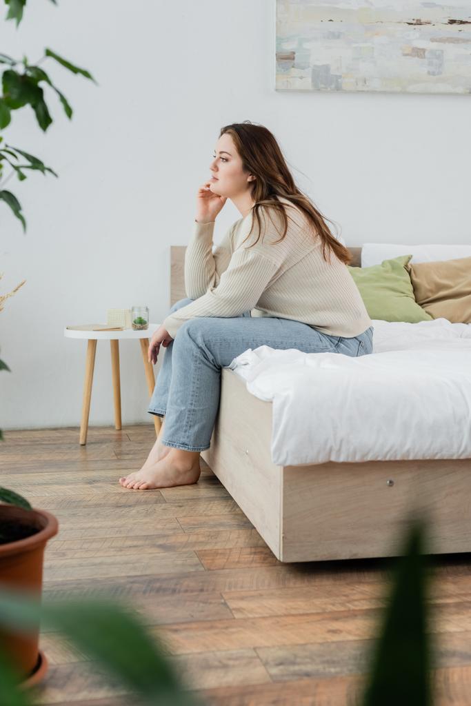 Πλευρική άποψη του νεαρού σώματος θετική γυναίκα κάθεται στο κρεβάτι στο σπίτι  - Φωτογραφία, εικόνα