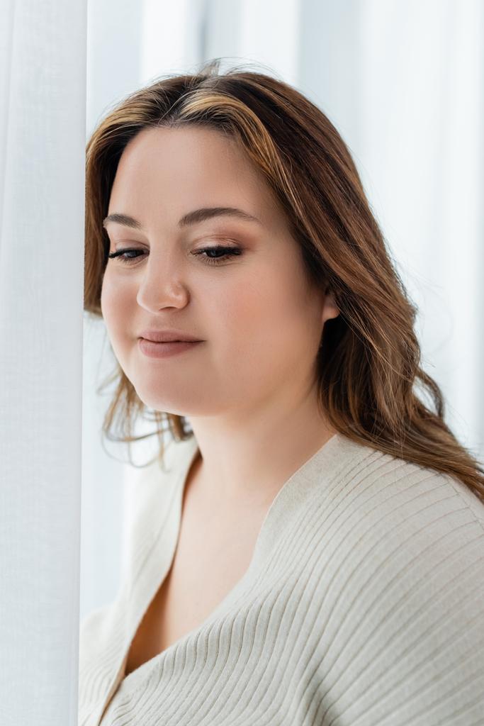 Pretty body positive woman standing near curtains at home  - Photo, Image