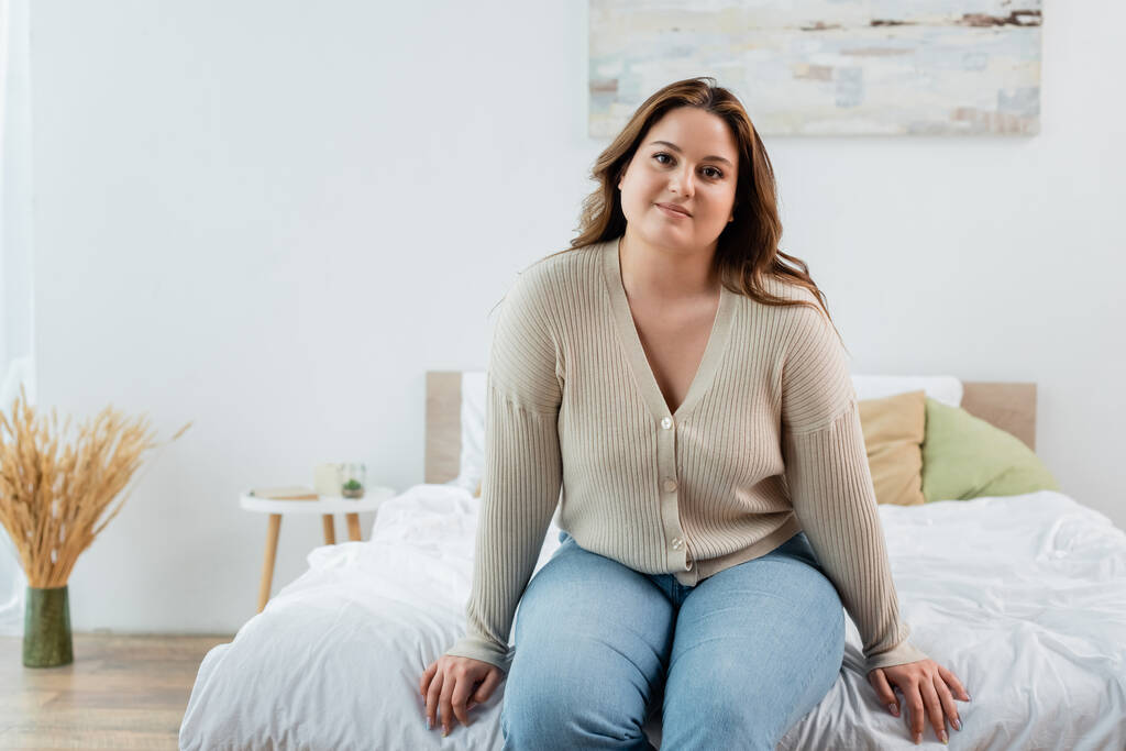 Χαμογελαστή γυναίκα με υπέρβαρο κάθεται στο κρεβάτι στο σπίτι  - Φωτογραφία, εικόνα