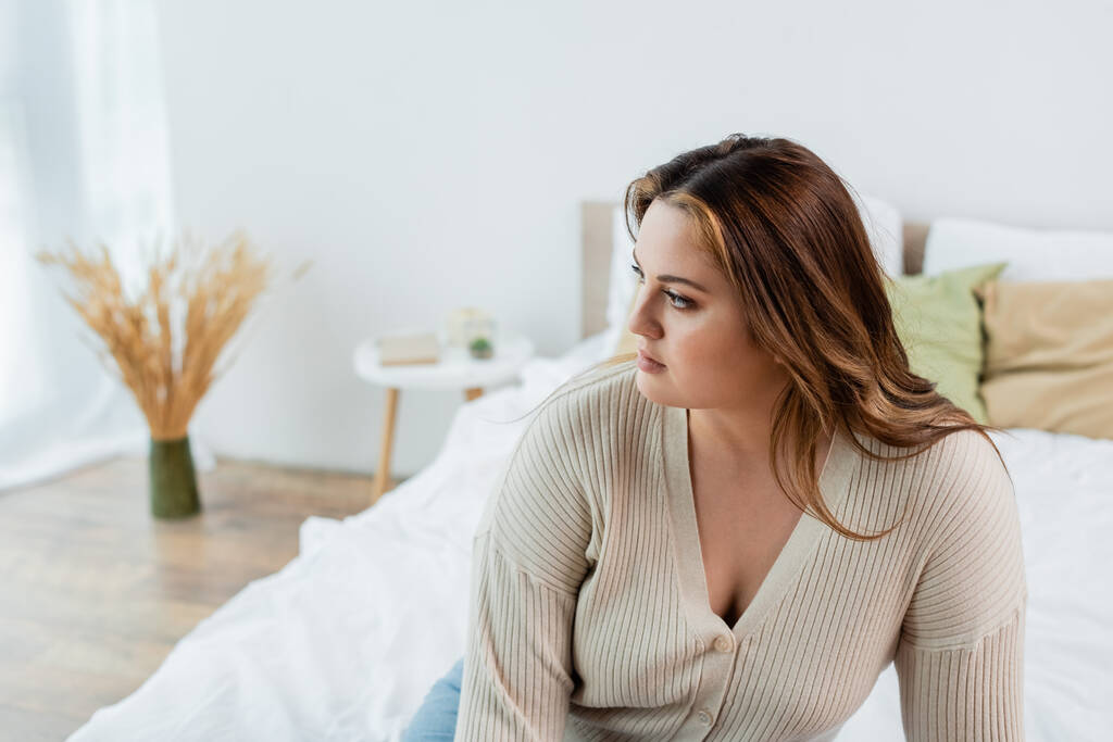 Mladá žena s nadváhou dívá pryč na rozmazané posteli doma  - Fotografie, Obrázek