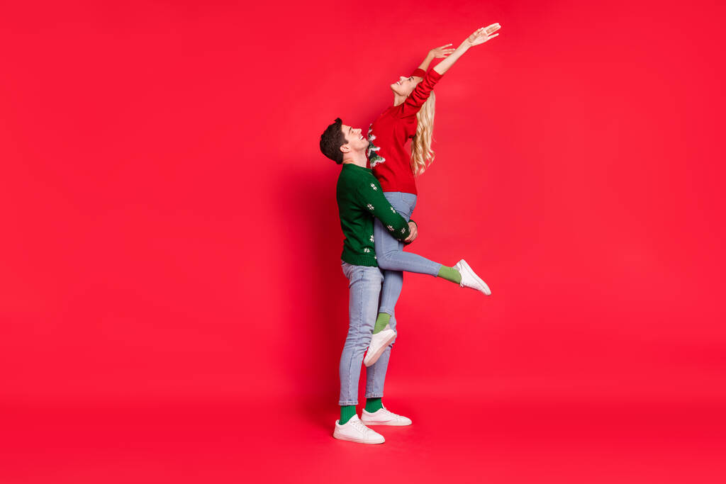 Повна довжина тіла фото хлопець тримає насолоджуючись щасливою дівчиною в різдвяних нарядах ізольований яскраво-червоний кольоровий фон
 - Фото, зображення