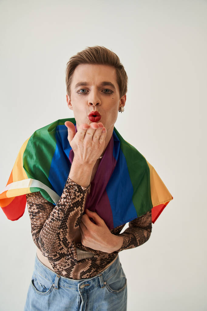 Feminine male wrapped at the lgbt flag sending air kiss to the camera while posing - Photo, Image