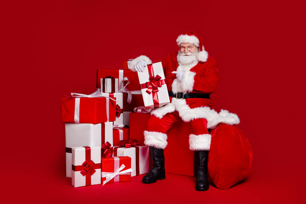 Çekici, yakışıklı, emekli bir adamın Noel Baba kostümlü fotoğrafı izole edilmiş kırmızı arkaplanı gösteren bir gülümseme sunar. - Fotoğraf, Görsel