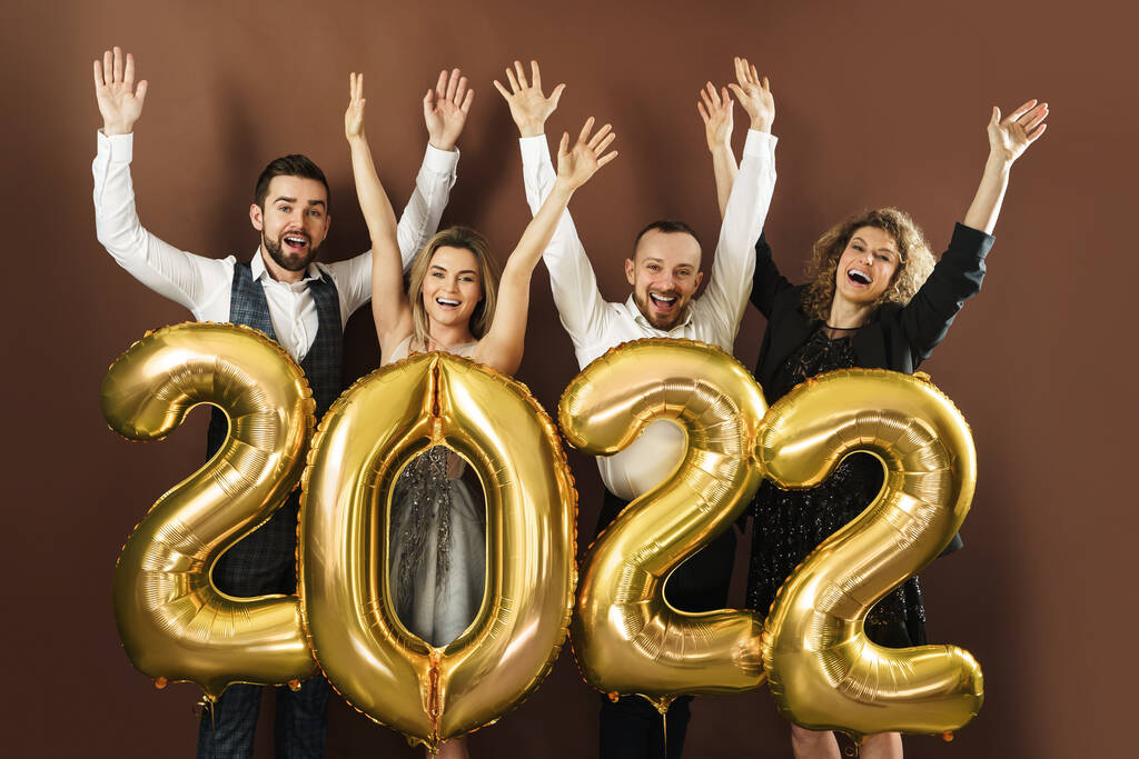 Ryhmä kauniita hyvin pukeutunut puolue ihmiset juhlivat saapumista 2022 uudenvuoden kultainen ilmapalloja ruskea tausta - Valokuva, kuva