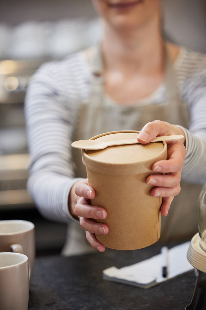 close-up van vrouwelijke werknemer in cafe serveren maaltijd in duurzame recycleerbare verpakking met houten lepel - Foto, afbeelding
