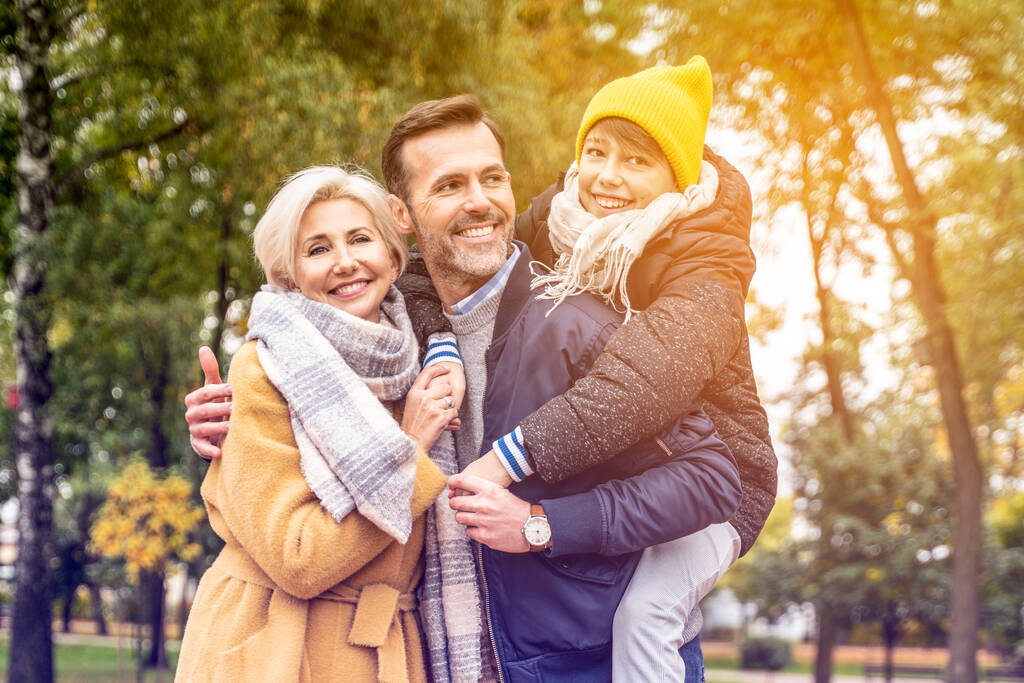 Prawdziwi ludzie koncepcja stylu życia i emocji rodzinnych - szczęśliwa mama, tata i syn bawią się razem, spacerują po jesiennym parku - Zdjęcie, obraz