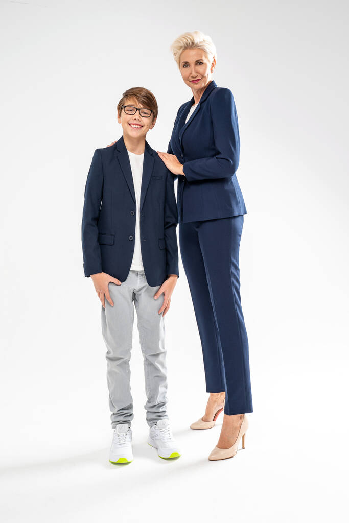 Muttertagskonzept - hübscher Teenie-Junge posiert mit seiner eleganten Mutter auf weißem Studiohintergrund mit viel Kopierraum. Frau zeigt stolz auf ihren Sohn - Foto, Bild