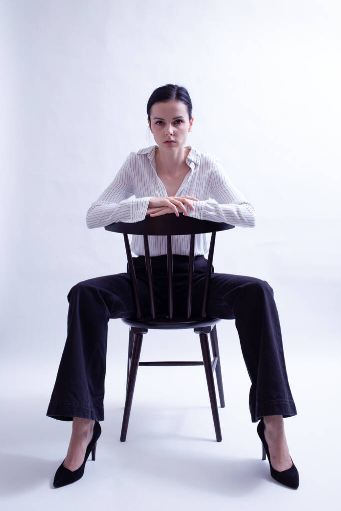 Frau in weißem Hemd und schwarzer Hose sitzt auf einem Stuhl - Foto, Bild