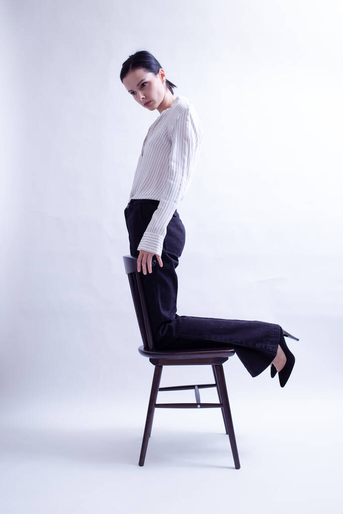 жінка в білій сорочці і чорні штани сидить на стільці
 - Фото, зображення