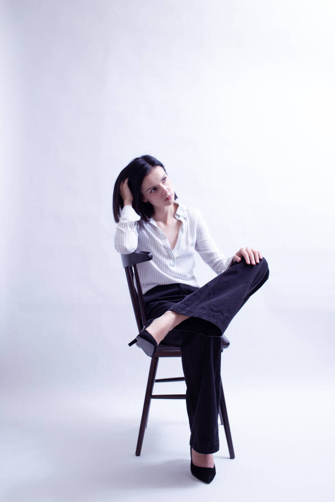 vrouw in wit shirt en zwarte broek zit op een stoel - Foto, afbeelding