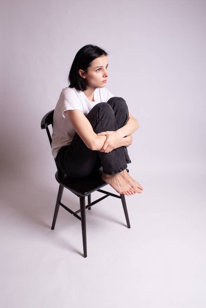 Το κορίτσι με το άσπρο μπλουζάκι κάθεται σε μια καρέκλα στο στούντιο - Φωτογραφία, εικόνα