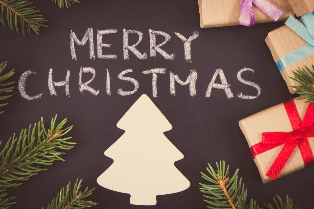 Decoratie voor Kerstmis. Inscriptie Vrolijk kerstfeest, ingepakte cadeaus met lint, kerstboomvorm en groene sparren takken op zwarte achtergrond - Foto, afbeelding