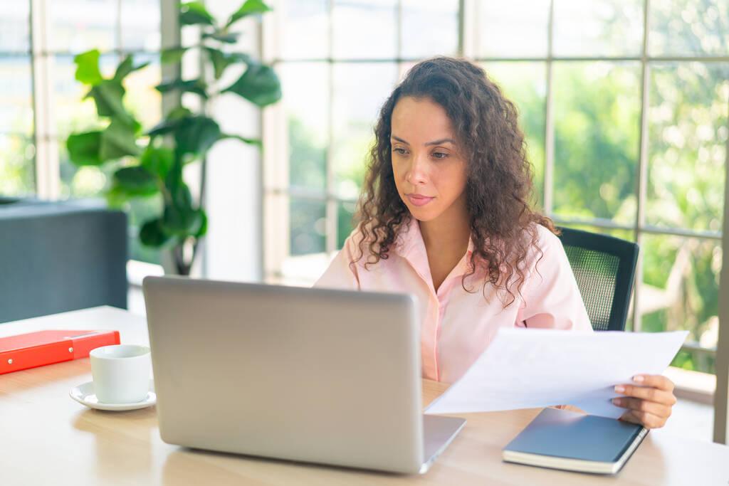 Femme latine travaillant avec un ordinateur portable et du papier sur l'espace de travail à la maison - Photo, image