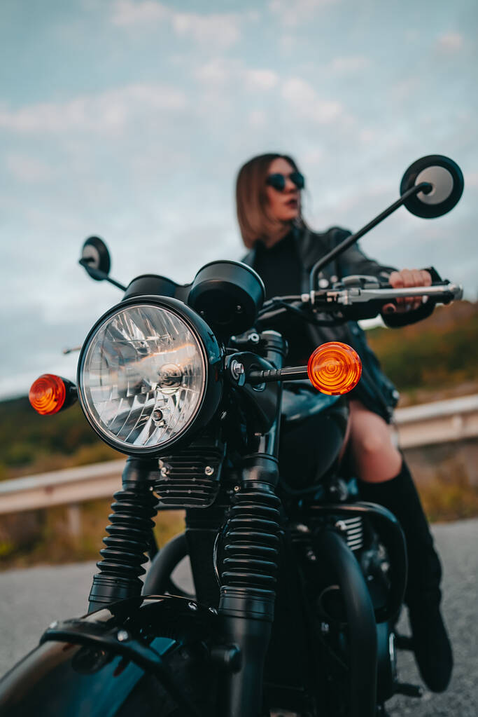 Motocyklistka siedząca na motocyklu w stylu retro. Seksowna kobieta w butach na jezdni. Wycieczka, prędkość, koncepcja wolności. - Zdjęcie, obraz