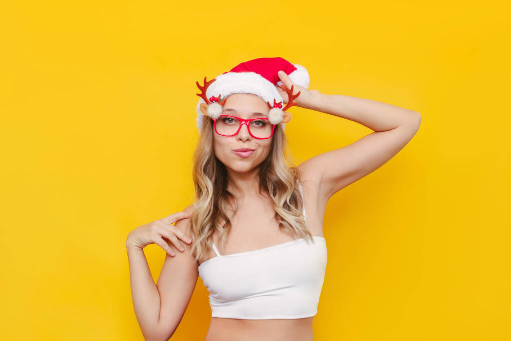 beautiful young woman in santa claus hat and glasses on yellow background - Photo, Image