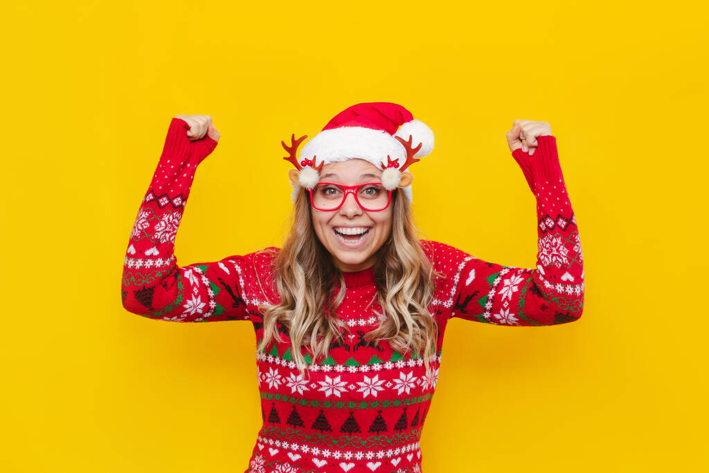 fiatal gyönyörű nő visel karácsonyi kalap és szemüveg elszigetelt sárga háttér ünneplő győzelem és a siker nagyon izgatott, meglepett - Fotó, kép