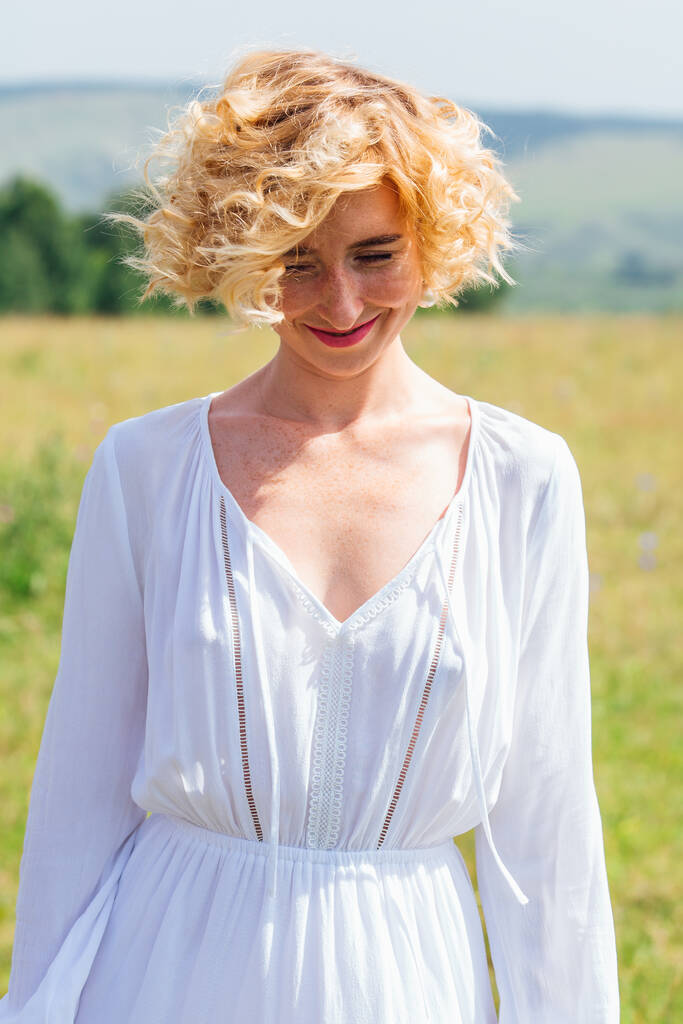Beautiful blonde woman with short curly hair outdoors. Romantic model in summer white dress. - Photo, Image