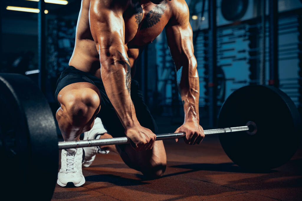Close-up young man, muscled athlete, bodybuilder with heavy barbell at sport gym, indoors. Concept of sport, activity, healthy lifestyle - Photo, Image