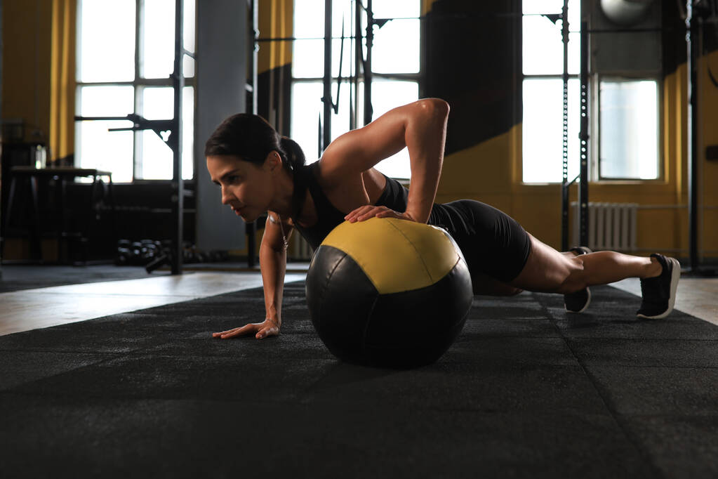 Formda ve kaslı bir kadın spor salonunda ilaç topuyla egzersiz yapıyor. - Fotoğraf, Görsel
