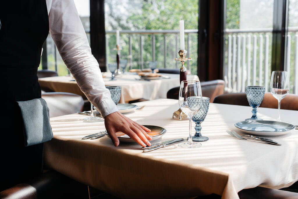 Ein junger Kellner in stylischer Uniform bedient den Tisch in einem schönen Gourmetrestaurant in Großaufnahme. Restaurantbetrieb auf höchstem Niveau. - Foto, Bild