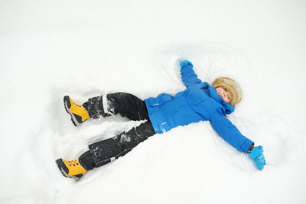 Top view of child doing snow angel. Little boy playing in snowdrift and having fun with fresh snow. Active outdoors leisure for kids on nature in snowy winter day. - Photo, Image