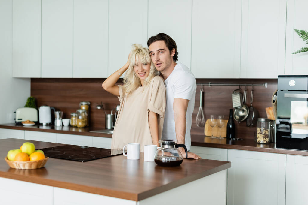 femme heureuse ajustement cheveux blonds près du petit ami dans la cuisine  - Photo, image