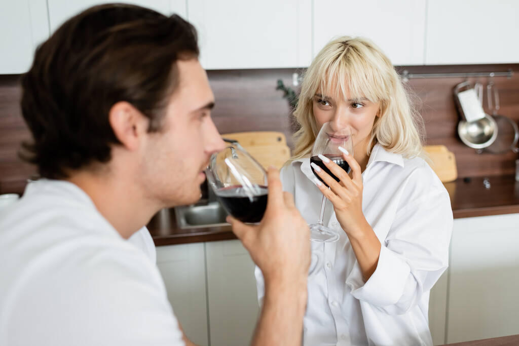mulher loira bebendo vinho tinto e olhando para o namorado borrado  - Foto, Imagem