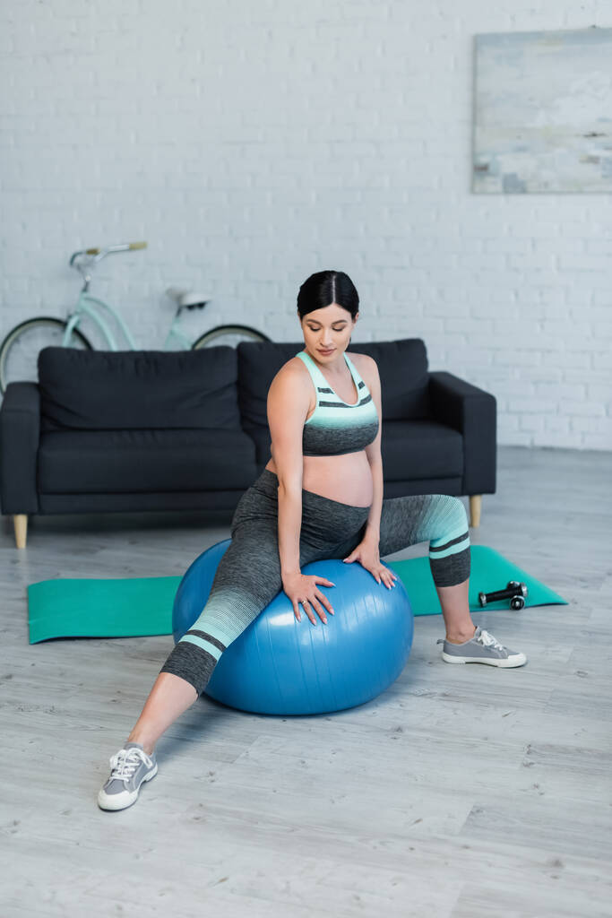 jonge zwangere vrouw in sportkleding training op fitness bal thuis - Foto, afbeelding