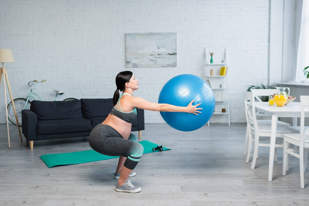 oldalnézetben terhes nő csinál felülések fitness labda asztal mellett friss narancslé - Fotó, kép