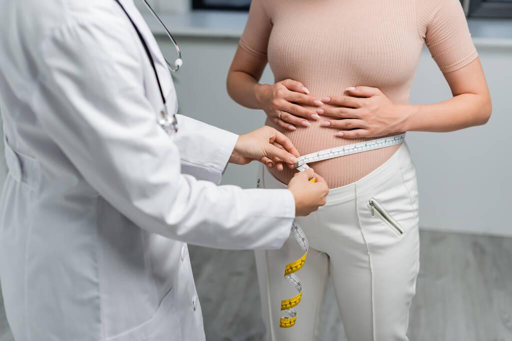 vista recortada de la mujer embarazada cerca del médico midiendo su vientre en la clínica - Foto, Imagen