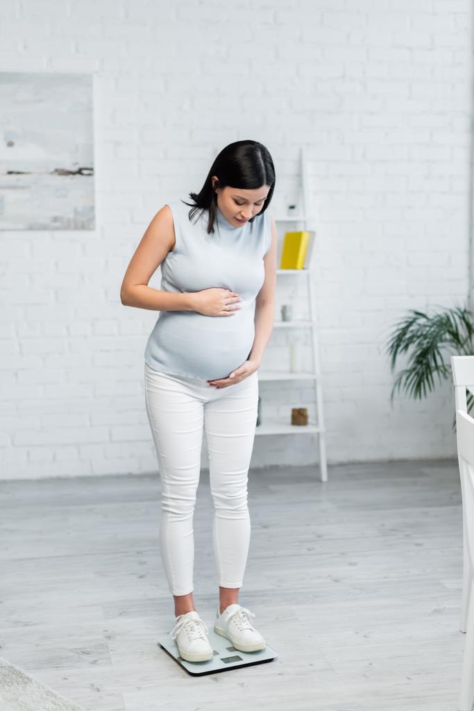 vista completa de la mujer embarazada midiendo el peso corporal en básculas de piso en casa - Foto, Imagen