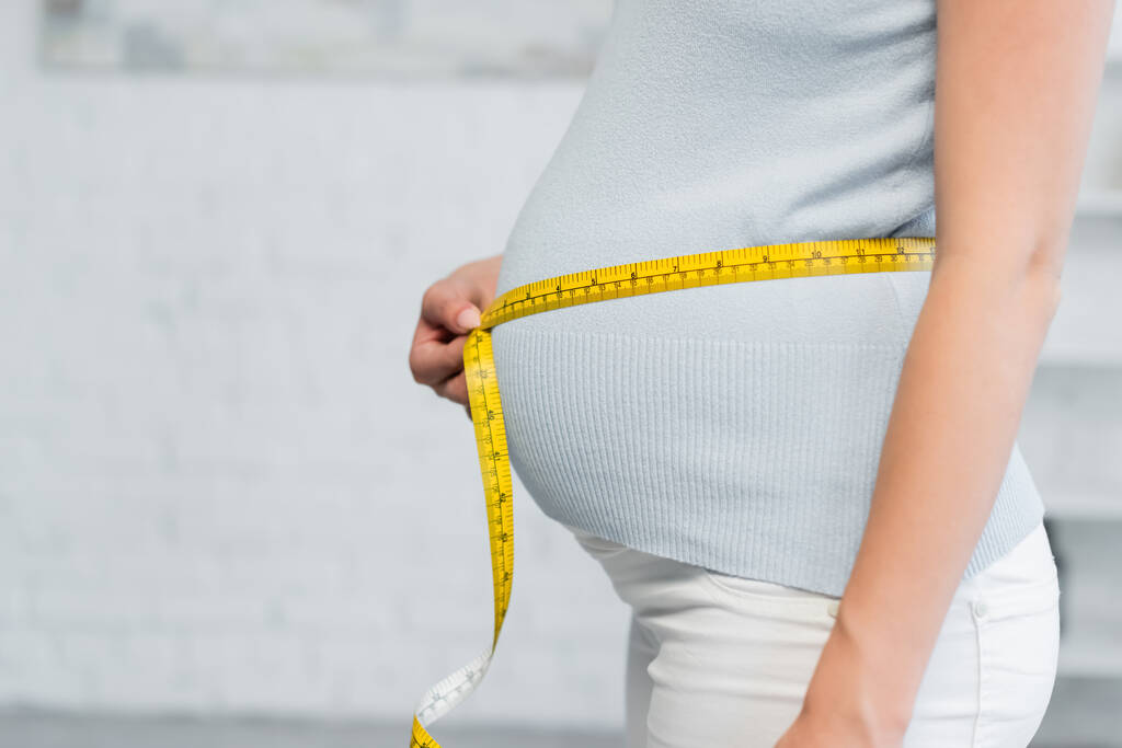 vista parziale della donna incinta stima delle dimensioni della pancia con nastro di misurazione - Foto, immagini