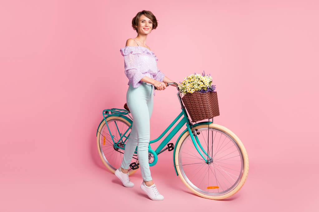 Photo pleine grandeur de jeune fille heureuse positive souriante souriante tenir vélo avec des fleurs sauvages isolé sur fond de couleur rose - Photo, image