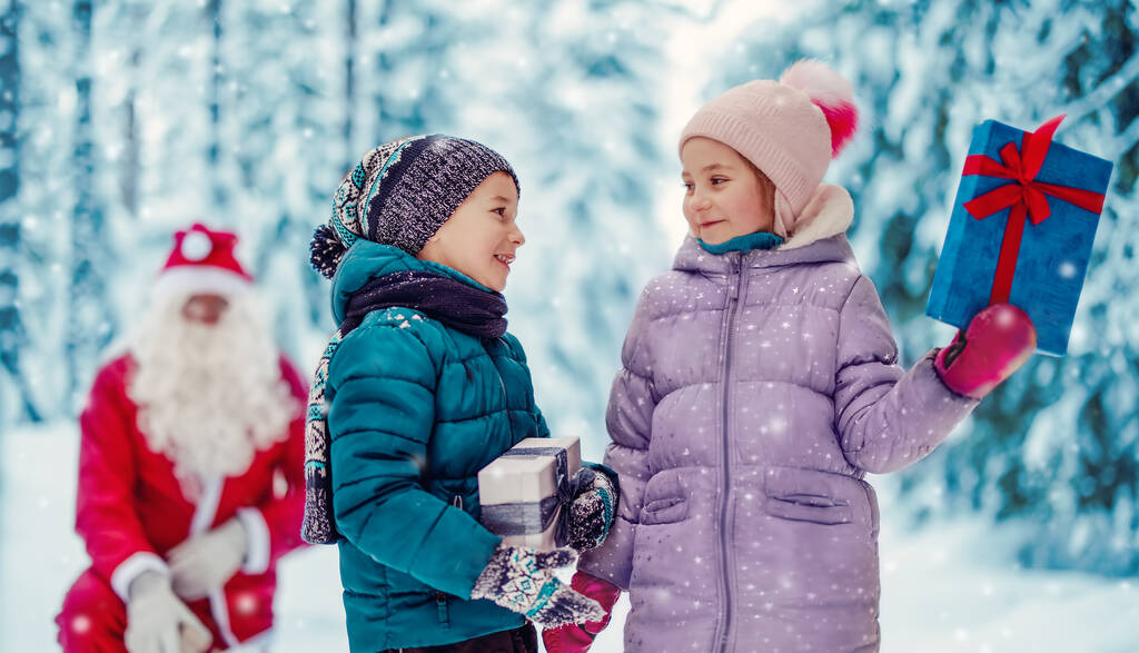 サンタクロースは雪の公園の子供のためのいくつかの現在のボックスを与える - 写真・画像