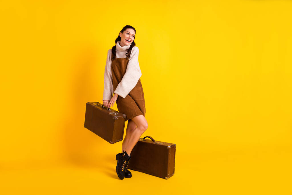 Pleine longueur photo de dame mignonne excitée habillée brun tenant globalement deux valise à la recherche d'espace vide isolé fond de couleur jaune - Photo, image