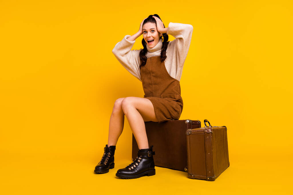 Çekici, şen şakrak bir kızın, parlak sarı arka planda izole edilmiş bir şekilde çantalara oturup eğlenmesi. - Fotoğraf, Görsel