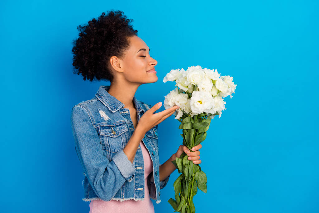 Photo de attrayant jeune femme afro américaine heureuse tenir les mains fleurs odeur isolé sur fond de couleur bleue - Photo, image