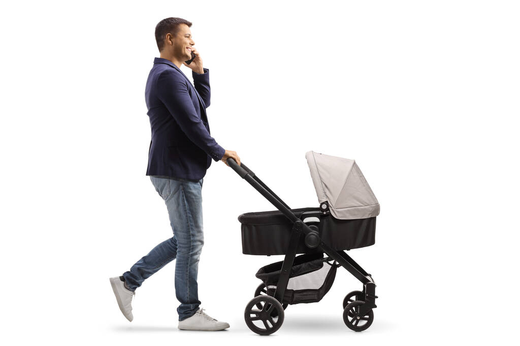 Full length profile shot of a father pushing a baby carriage and making a phone call isolated on white background - Photo, Image