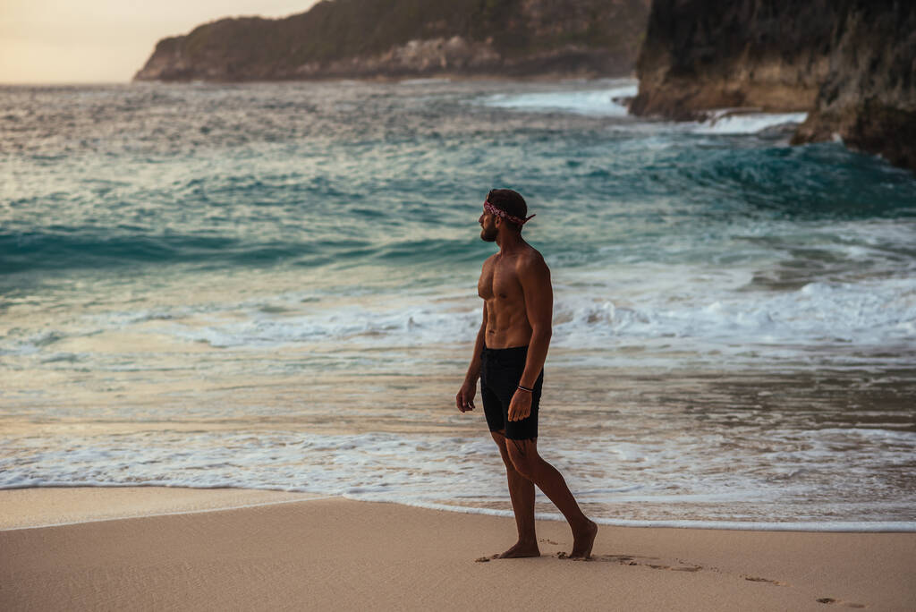 Mężczyzna z nagim tułowiem na wybrzeżu. Samotny mężczyzna stoi na plaży. Mężczyzna spotyka zachód słońca na plaży w Indonezji. Przestrzeń kopiowania - Zdjęcie, obraz