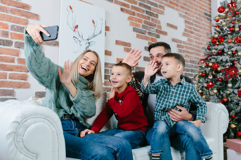 友人や家族と話すスマートフォンを使用して2人の子供と美しい幸せな結婚したカップルは、ビデオ通話会議アプリでメリークリスマスを祝います。現代技術新年2022のおめでとうございます。. - 写真・画像