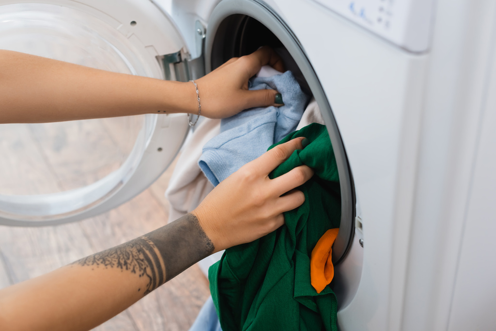 częściowy widok wytatuowanej kobiety wkładającej pranie do pralki - Zdjęcie, obraz