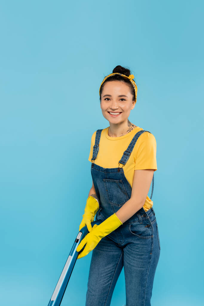 cheerful housewife with vacuum cleaner smiling at camera isolated on blue - Photo, Image