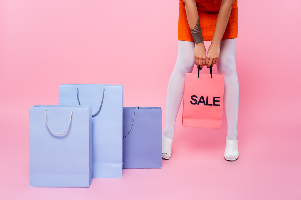 ピンクの購入の近くに販売レタリング付きショッピングバッグを保持している入れ墨の女性の部分的なビュー - 写真・画像