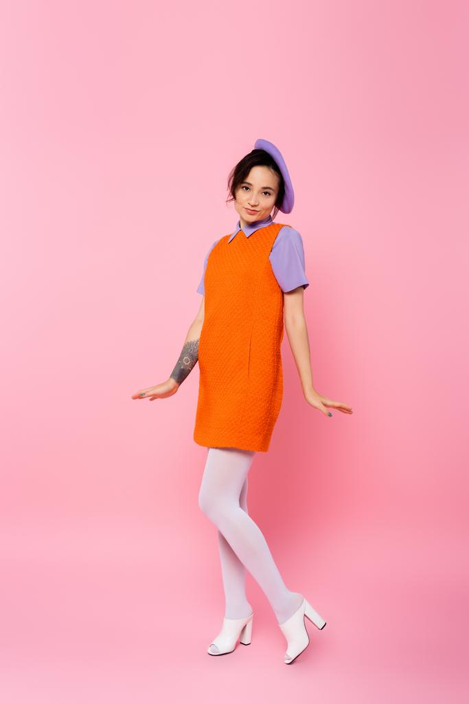 vista completa de la mujer positiva en vestido naranja sin mangas posando en rosa - Foto, imagen