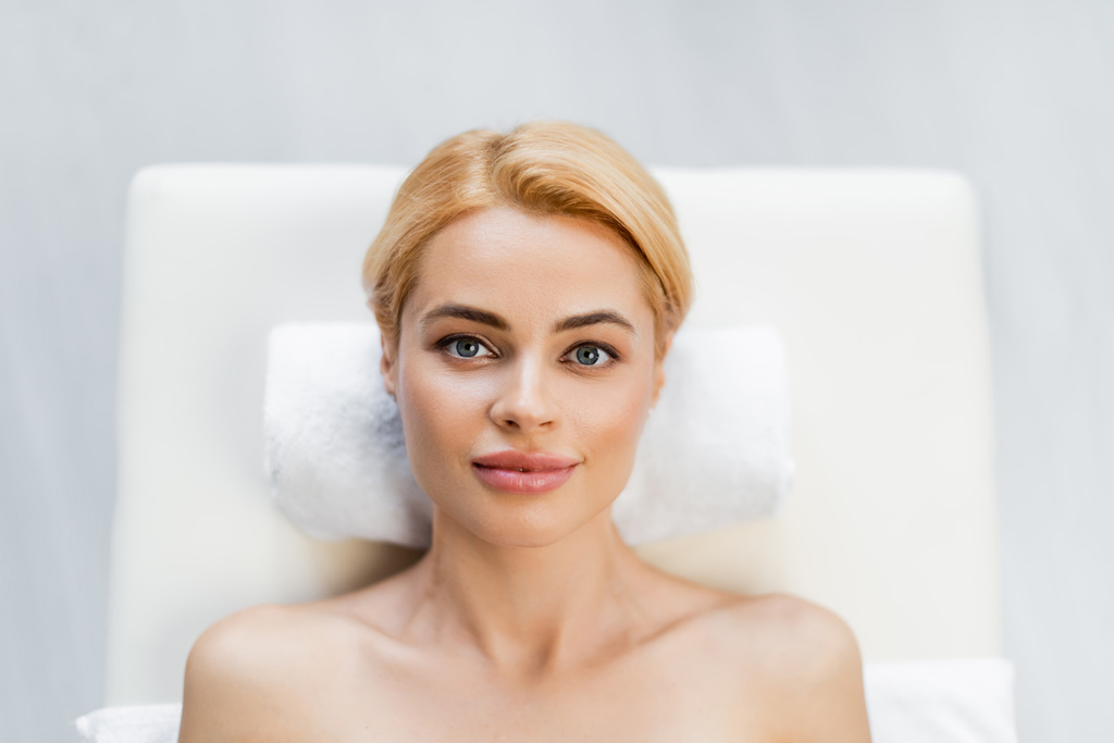 vista superior del cliente rubio con hombros desnudos acostado en la mesa de masaje en el centro de spa  - Foto, Imagen