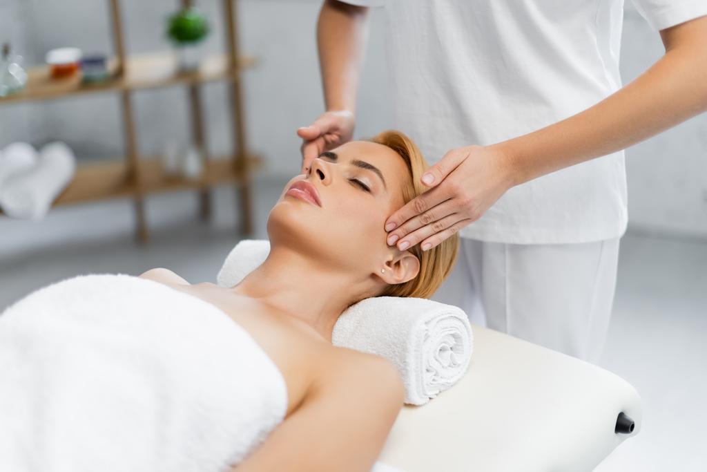 massagista fazendo massagem na cabeça de cliente loiro com olhos fechados  - Foto, Imagem