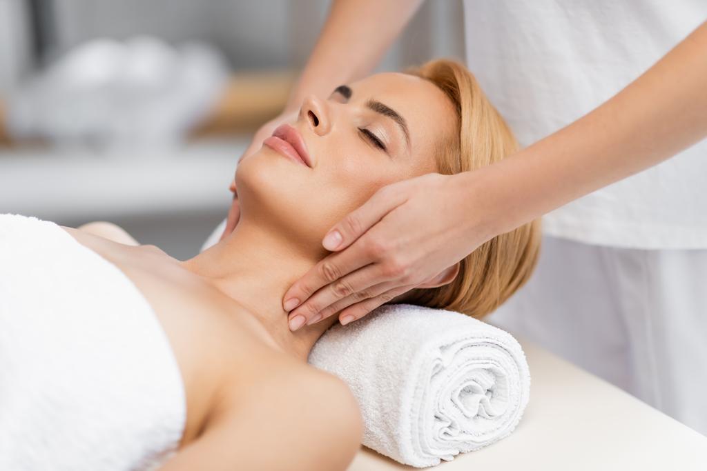 blond client met gesloten ogen ontvangst nek massage in spa centrum - Foto, afbeelding