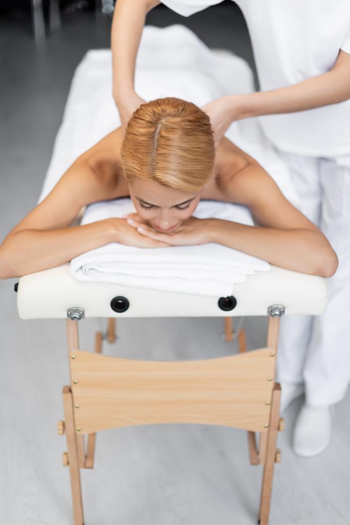 masajista haciendo masaje de espalda a cliente rubio con los ojos cerrados  - Foto, Imagen